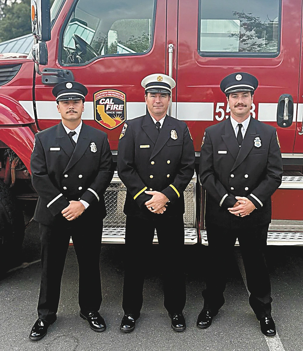 Three men in dark uniforms with badges stand in front of a red CAL FIRE fire truck marked 543 on pavement.