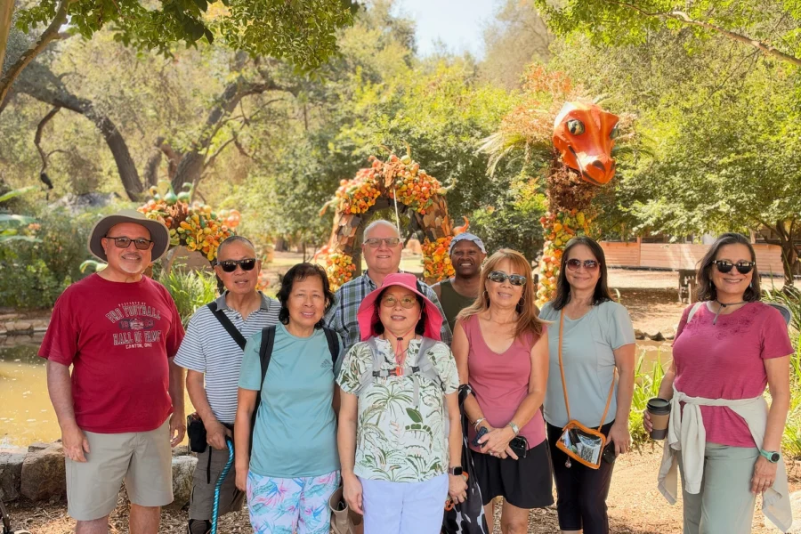 Group of people posing for photo under trees near colorful sculpture.