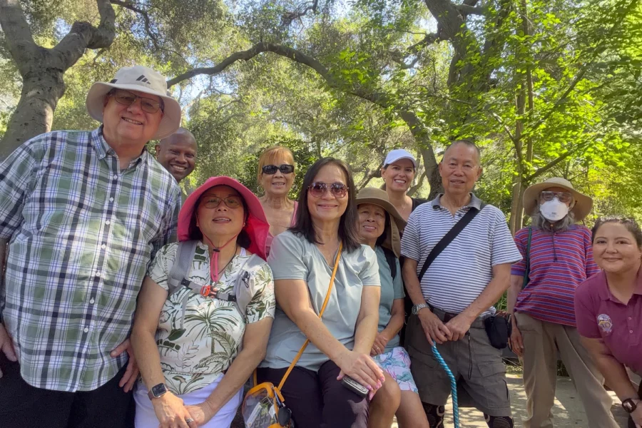 Group of people posing together under leafy trees in a sunny park.