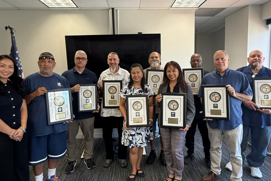 Group of people holding framed awards in an office with an American flag.