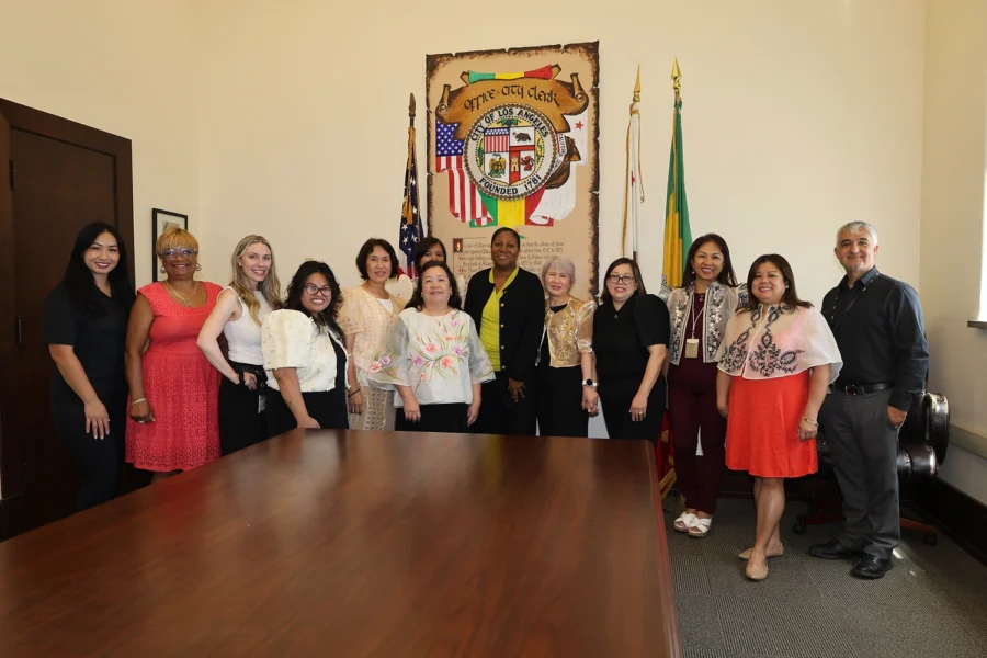 Group of people posing for a photo in an office with a large table, city clerk banner, and flags.