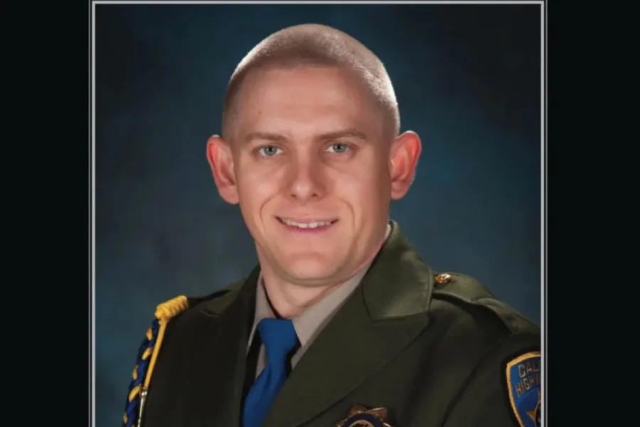 Man in uniform with badge, smiling, against blue background.