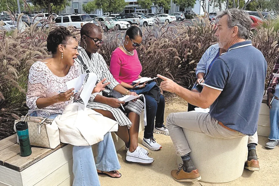 Group of people seated outdoors, engaged in conversation near a modern building.