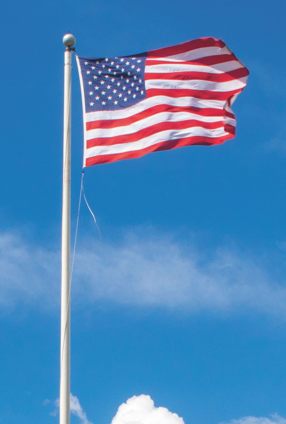 American flag on a white pole, waving against a blue sky with scattered clouds.